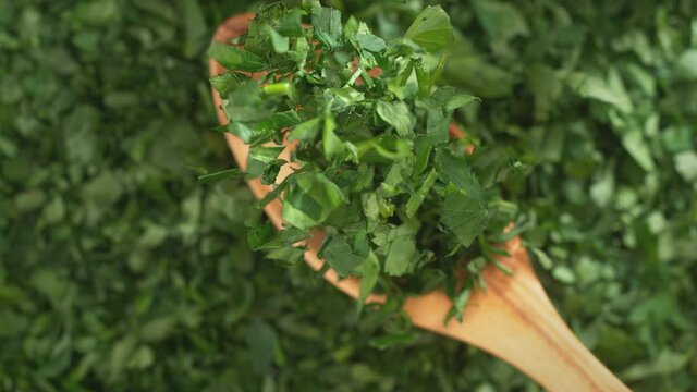 Olive Wood Spoon with Chopped Parsley Falling onto Green Herbs in Slow Motion (Phantom Flex)