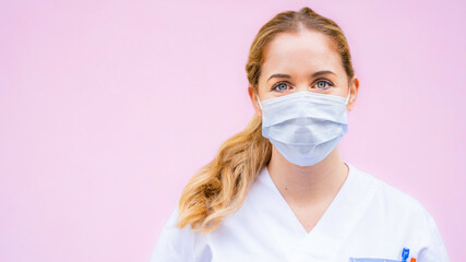 close up of a beautiful young nurse ready to work with surgical mask on a light green background looking straight into camera