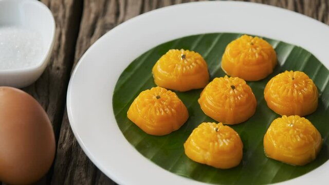 Woman's hand is delicately placing Thong-Ek (Thai Traditional dessert) on a white plate with banana leaves.