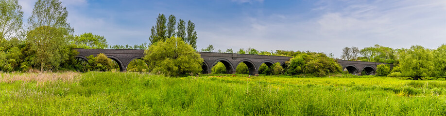 Fototapeta na wymiar A panorama view along the banks of the River Nene towards the old railway viaduct at Thrapston, UK in springtime