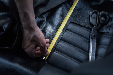 Selective focus shot of a tailor measuring and cutting leather for car seats
