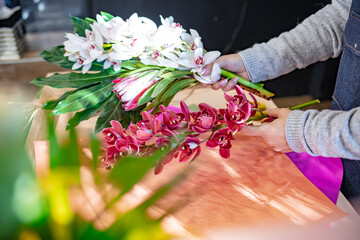 Florist at work: pretty young woman making fashion modern bouquet of different flowers. Smiling lovely young woman florist arranging plants in flower shop