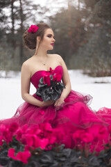 A beautiful girl in a pink ball gown with lots of cyclamen flowers on the snow background
