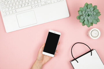 Shopping Online Concept. Womens hands with phone and laptop on pink background. Top view, copy space.