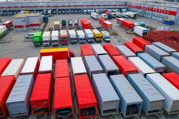Cargo containers stand on the parking lot of the logistics terminal. Freight containers with semi-trailers trucks stand outside the warehouse in loading hub. Aerial view