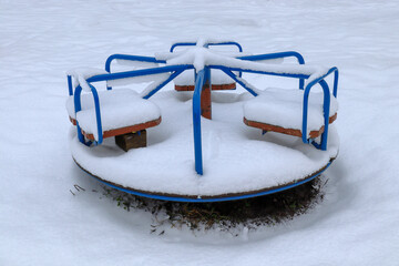 Snow-covered round carousel for children on the playground in winter. Equipment for children.