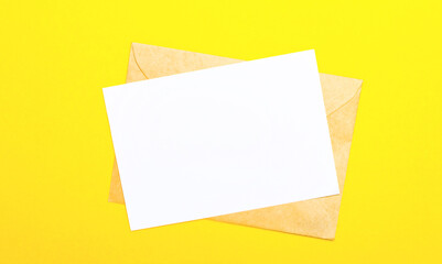 On a yellow-colored background, an envelope and a blank card with space to insert text or illustrations. Top view with copy space