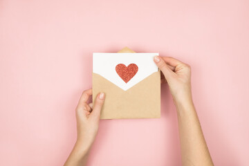 Love letter in women hands on Valentines Day. Handmade postcard with red heart on pink background....