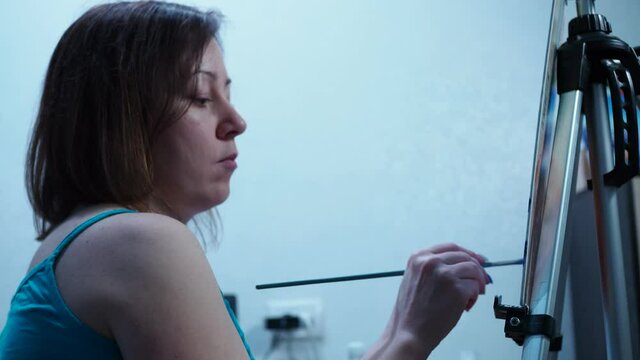 a girl draws a brush on a canvas standing on a tripod.