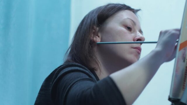 the artist draws a brush on a canvas standing on a tripod. home studio of fine arts. view of the girl from the bottom.