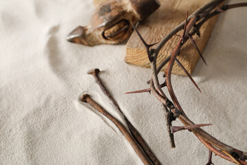 Crown of thorns, wooden plank and hammer with nails on sand. Easter attributes