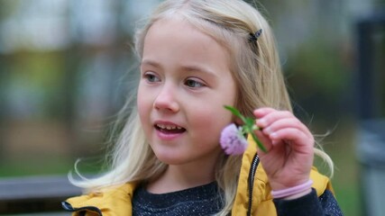 Portrait of a lovely little girl holds a clover flower in his hands. cute girl 5 years old cunning eyes looking away with a smile look at camera. close up Shot video. Slow motion footage