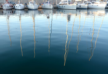 Reflections of trees of sailboats in the waters of the marina of San Remo in Liguria