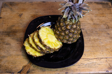 Sliced ​​pineapple on a black plate on a wooden table