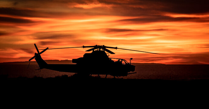 Silhouette of an attack helicopter at against a dramatic cloudy sky at sunset or sunrise - Powered by Adobe
