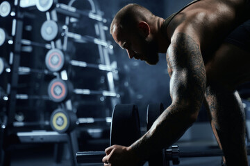Fototapeta na wymiar Muscular sportsman putting weights on barbell.