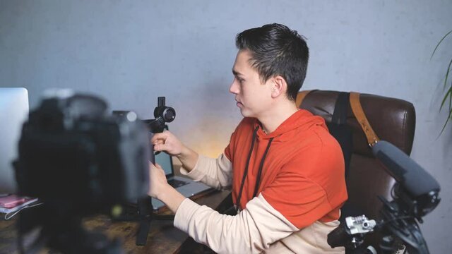 Young man sitting at the desk talking to the camera. Guy recording a video with professional equipments. Vlog, free lancer concept.