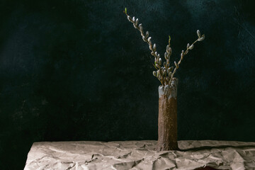 Spring mood still life with blossom willow branches in ceramic vase on table with crumpled craft paper. Dark background