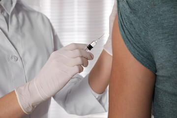 Doctor vaccinating man against Covid-19 in clinic, closeup