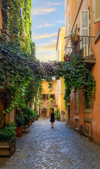 A solo female walks through an ivy covered colorful alley in the Trastevere district of Rome, Italy