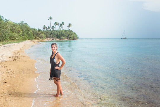Beautiful girl alone on beach in Spanish Virgin Islands traveling for vacation with palm trees and sailing catamaran sailboat anchored in background