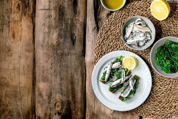 Appetizers tapas pickled anchovies or sardines fillet Wakame seaweed salad on toasted rye bread, served on blue plate with lemon on old wooden background. Flat lay, copy space.