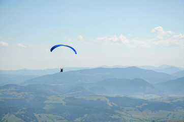 Paraglider flies in the sky over the mountains on a bright sunny day. Paragliding in the sky. Extreme sport.
