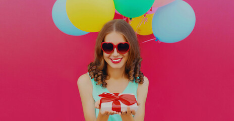 Portrait of happy young woman looking at gift box and colorful balloons on a pink background