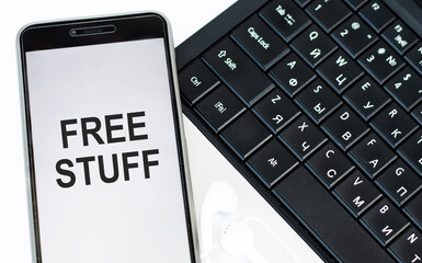 Text sign showing Free Stuff. Cell phone white screen with text on laptop keyboard background.