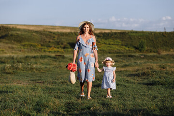 Young mother walking with her little daughter in the green field. Family holiday in garden. Portrait mom with child together on nature. Mum, little daughter outdoors. Happy Mothers Day. Close up.