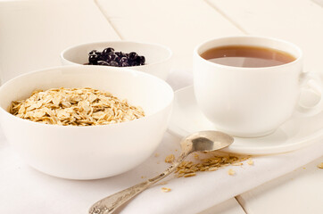 white cup of tea and a plate of oatmeal with currant jam on white background