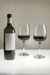 Vertical shot. Two large glasses with red wine and a bottle on a blurred background, close-up.