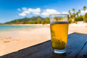 Sunny beach, and beer glass on wooden bar table. Ocean view with fresh beer on natural background.