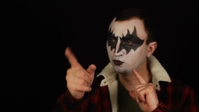 Man in scary demon makeup imitating guns, shooting into camera with finger pistols
