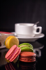 colorful macarons and cup of coffee over on black background.