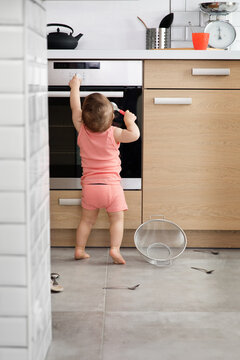 Rear view of toddler in kitchen touching oven knob