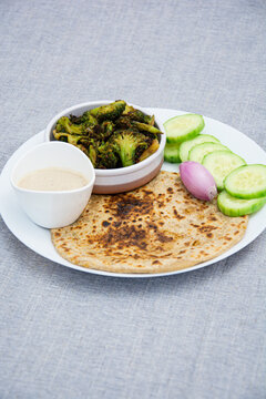 Aloo parotha in a white plate with onion, salad and broccoli fry with raita . An indian healthy breakfast