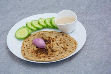 Aloo parotha in a white plate with onion, salad and broccoli fry with raita . An indian healthy breakfast