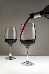 Red wine is poured from a bottle into a glass on a blurred background, close-up.