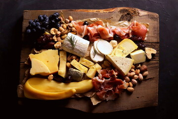 Aged varieties of cheese and different types of mold with dry-cured meats and nuts on a wooden board close-up selective focus.