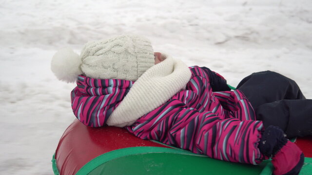 The Girl Is Being Rolled On An Inflatable Ring In The Snow. A Girl In Warm Clothes Lies On An Inflatable Ring And Is Pulled By A Rope By Another Person