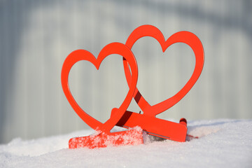 Closeup of bright red candlesticks in form of hearts on white soft snow in daylight on blurred background 