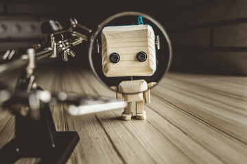 wooden robot android stands on a table under a magnifying glass. metal clamps with a magnifying...