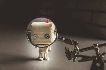 wooden robot android stands on a table under a magnifying glass. metal clamps with a magnifying glass. the face of a robot in the beautifying glass. human study concept