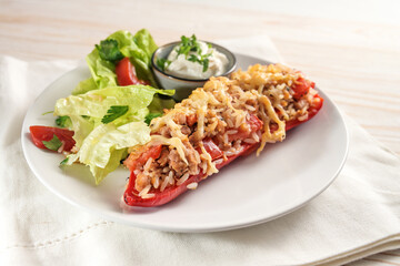 Pointed bell pepper baked with rice, tuna, tomatoes and cheese, lettuce salad, and dip, on a white plate and napkin, bright wooden table, copy space