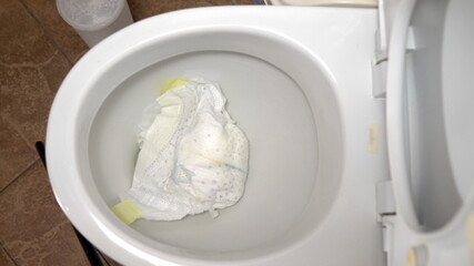 Close-up tossing a dirty baby diaper into the toilet. It clogs the toilet flush