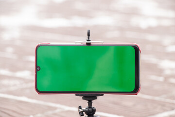 mobile phone with a green screen stands on a flexible stand on the road outside in winter
