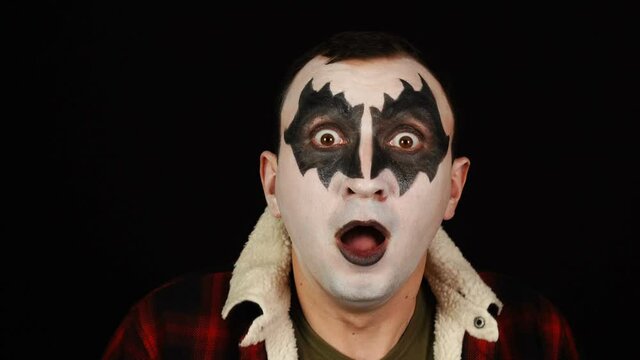 Emotionally scarred man in demon makeup is shocked on black background