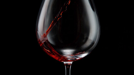 Naklejka na ściany i meble Pouring red wine into wine glass on a black background