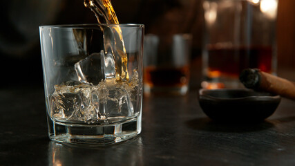 Glass of whisky with splashing liquid and ice rocks inside.